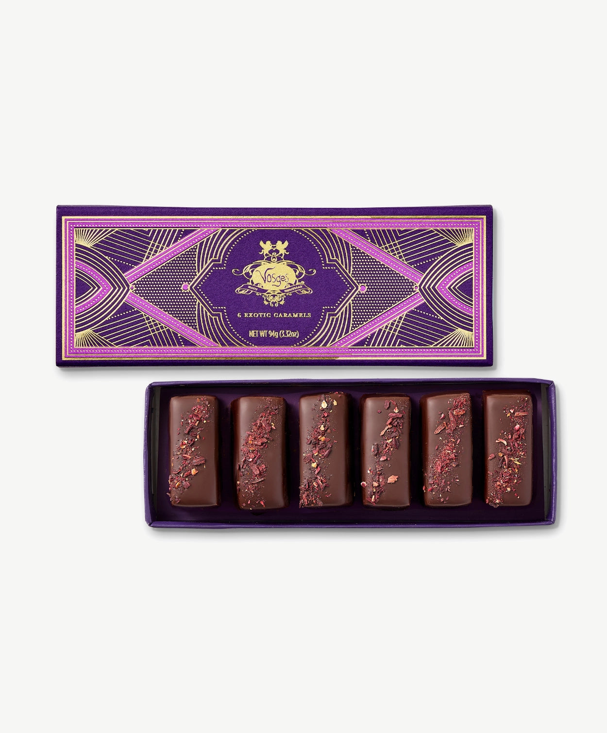 Six chocolate covered Vosges Caramels topped with hibiscus flowers in opened candy box embossed with gold foil on a grey background.