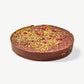 Closeup view of a Vosges Pistachio Marshmallow Chocolate Marshmallow disc topped with flecks of gold leaf, dried rose petals and pistachios on a white background.  