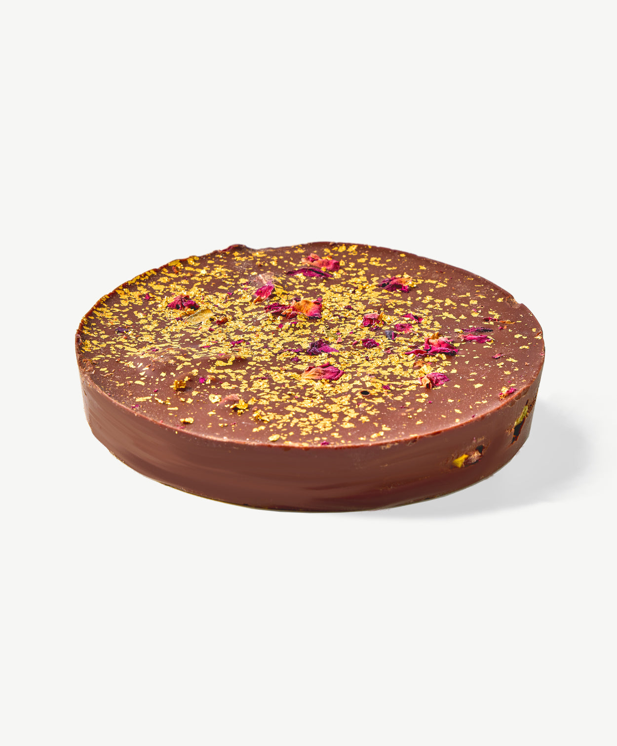 Closeup view of a Vosges Pistachio Marshmallow Chocolate Marshmallow disc topped with flecks of gold leaf, dried rose petals and pistachios on a white background.  