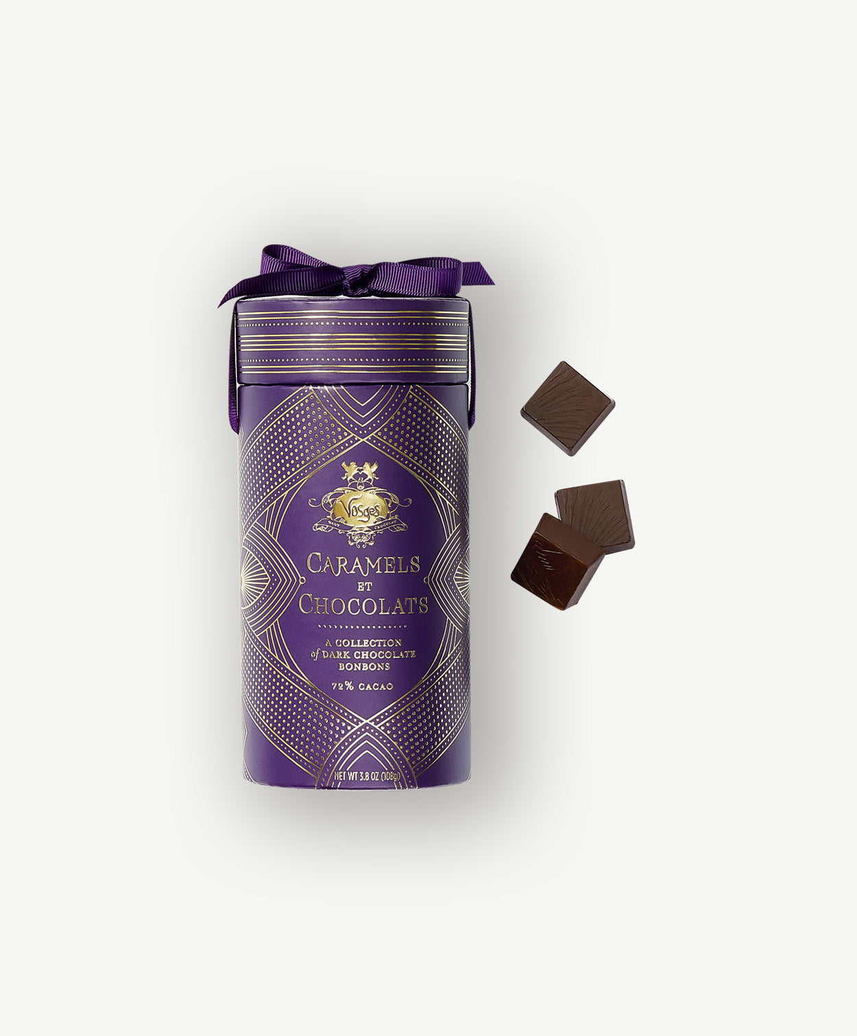 A tall purple tube embossed with the words, "Caramels et Chocolats" in gold foil, tied with a purple ribbon sit beside three chocolate covered caramels on a light grey background.