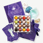 An open box of Vosges chocolate truffles adorned in brightly colored spices, nuts and dried flowers sits surrounded by crystals, precious stones, affirmation cards and meditation guide sit on a grey background.