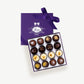 Purple chocolate box embossed with silver foil sits open displaying a Voges Italian Truffle collection with sixteen dark, milk and white chocolate bonbons on a grey background.  