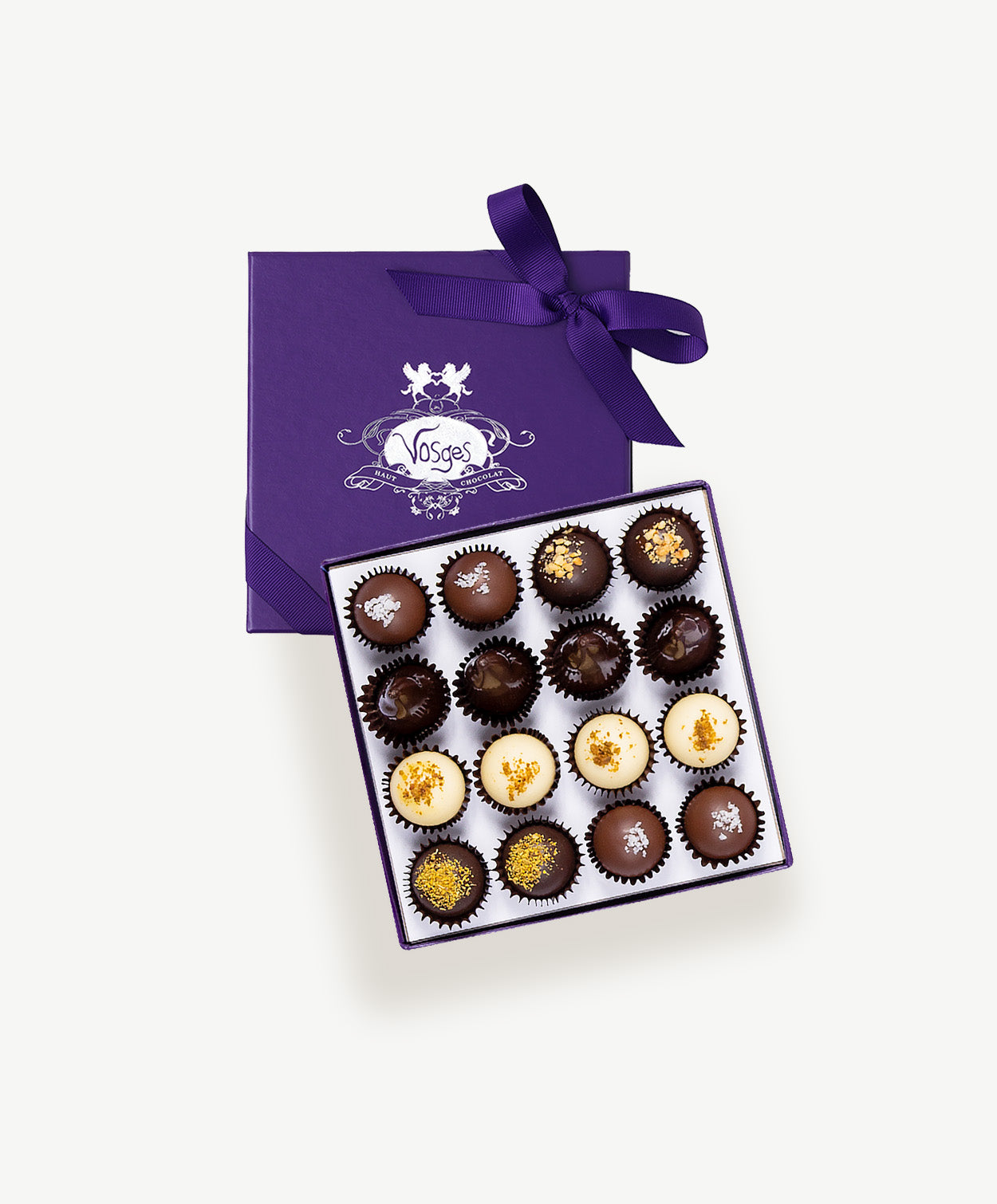 Purple chocolate box embossed with silver foil sits open displaying a Voges Italian Truffle collection with sixteen dark, milk and white chocolate bonbons on a grey background.  