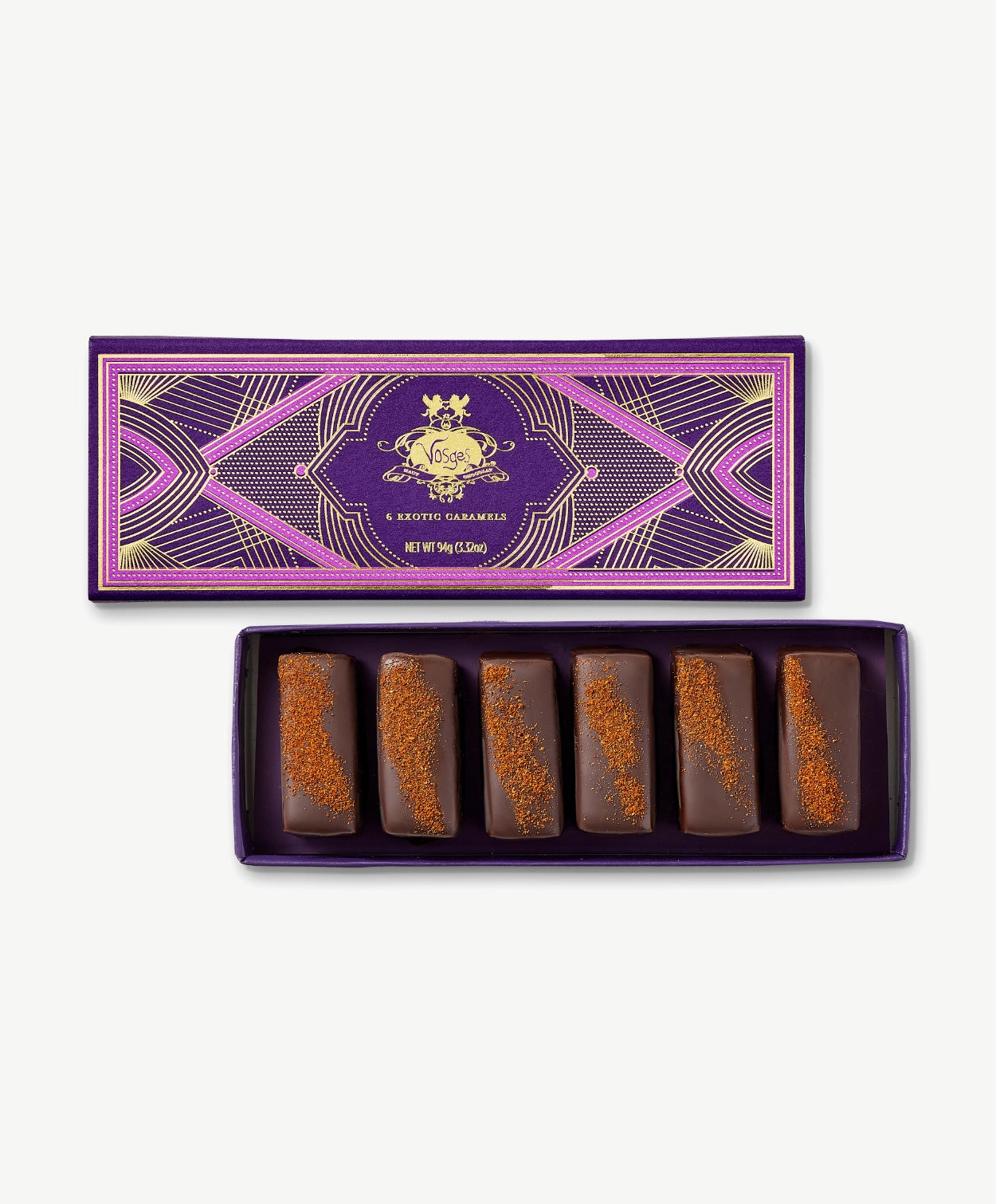 Six chocolate covered Vosges Caramels topped with Kokuto black sugar  in opened candy box embossed with gold foil on a grey background.