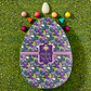 Egg-shaped purple candy box decorated in green dragons and several colorful Vosges chocolate truffles sit on a grass green background.
