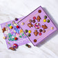Open box of chocolates and a painting of goddess Persephone surrounded by Vosges Haut-Chocolat Truffles on a grey marble slab.