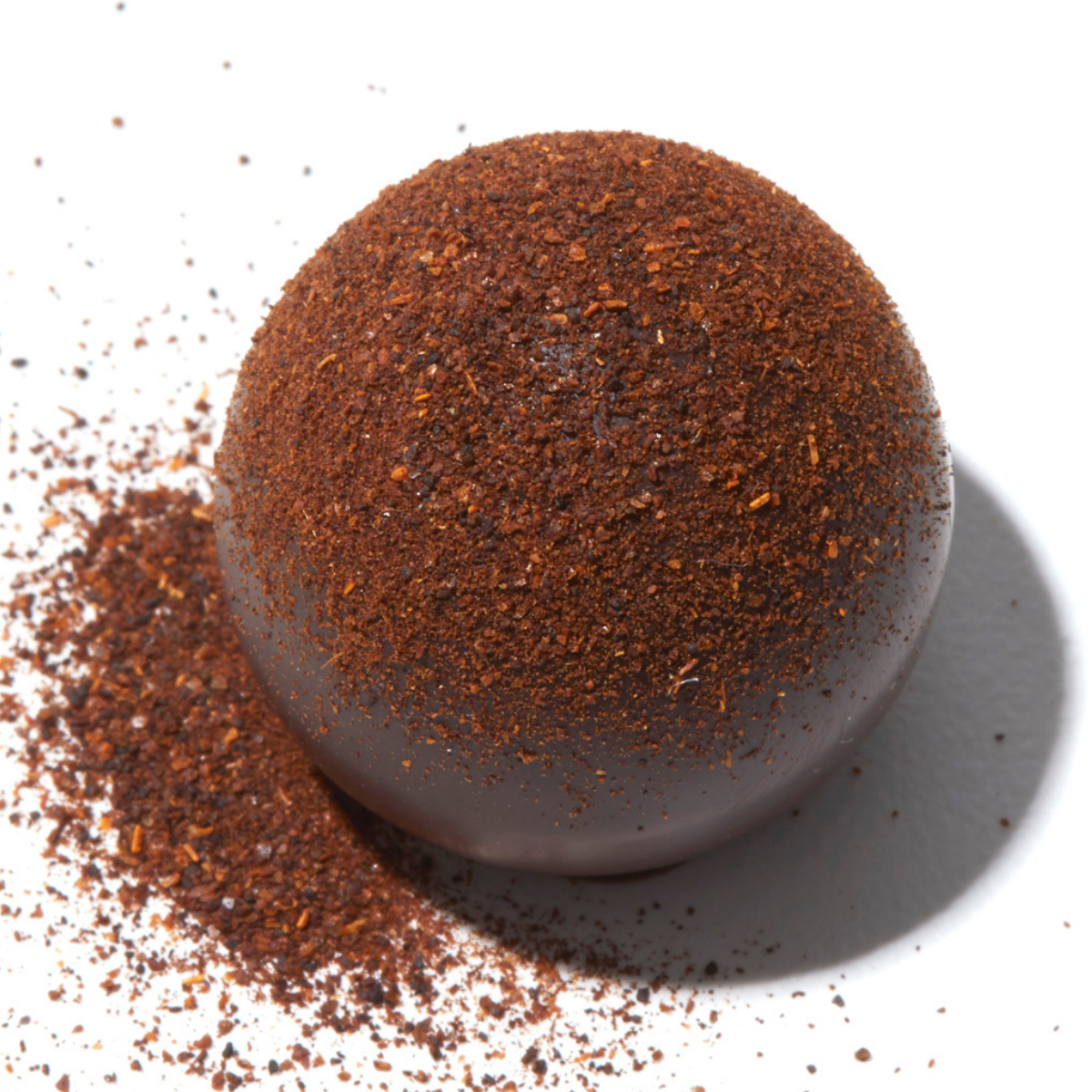 Close up view of a Vosges Red Fire truffle coated in dark chocolate and topped with Ancho chillies and Ceylon cinnamon on a white background.