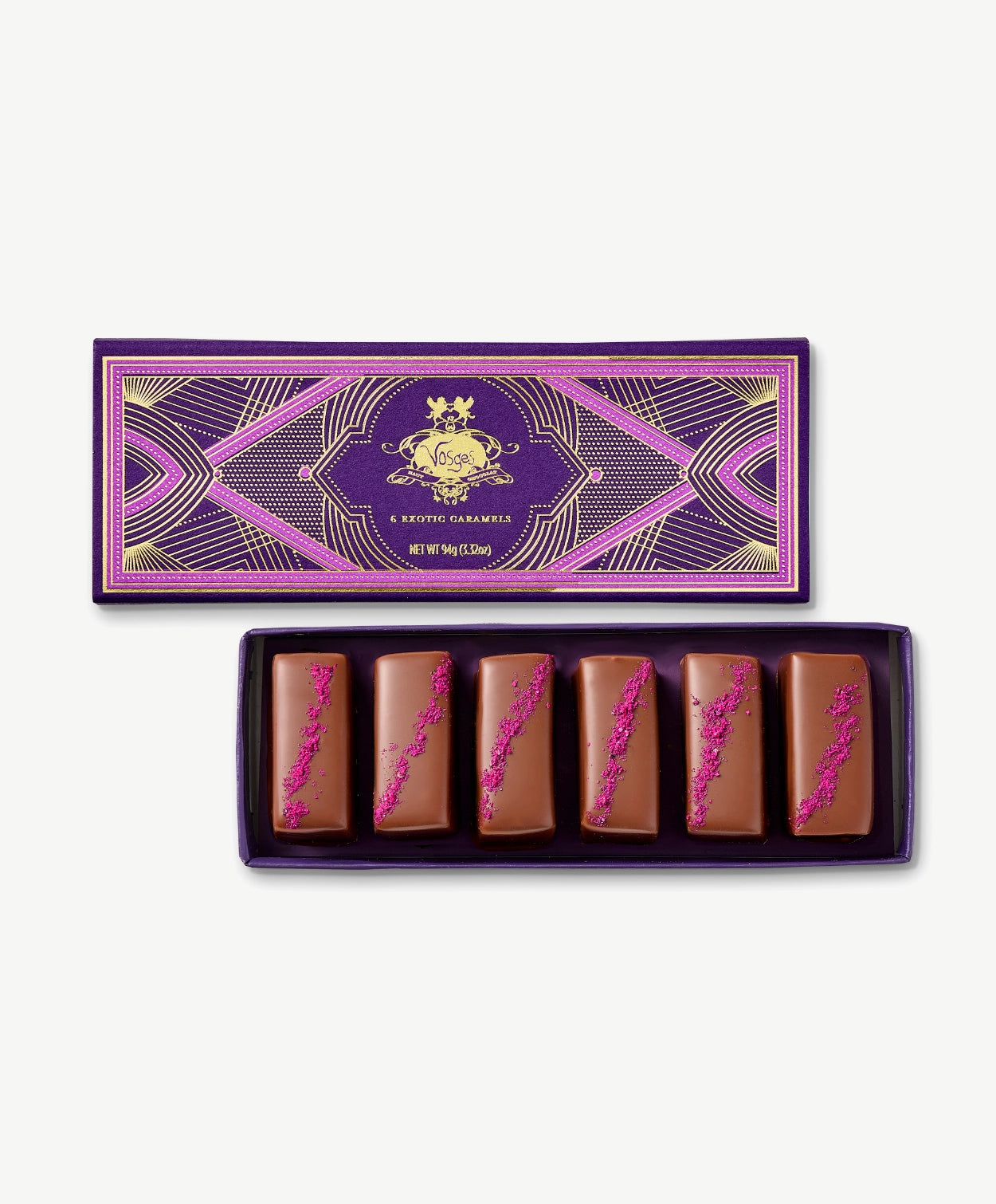 Six chocolate covered Vosges Caramels topped with red Hawaiian sea salt in opened candy box embossed with gold foil on a grey background.