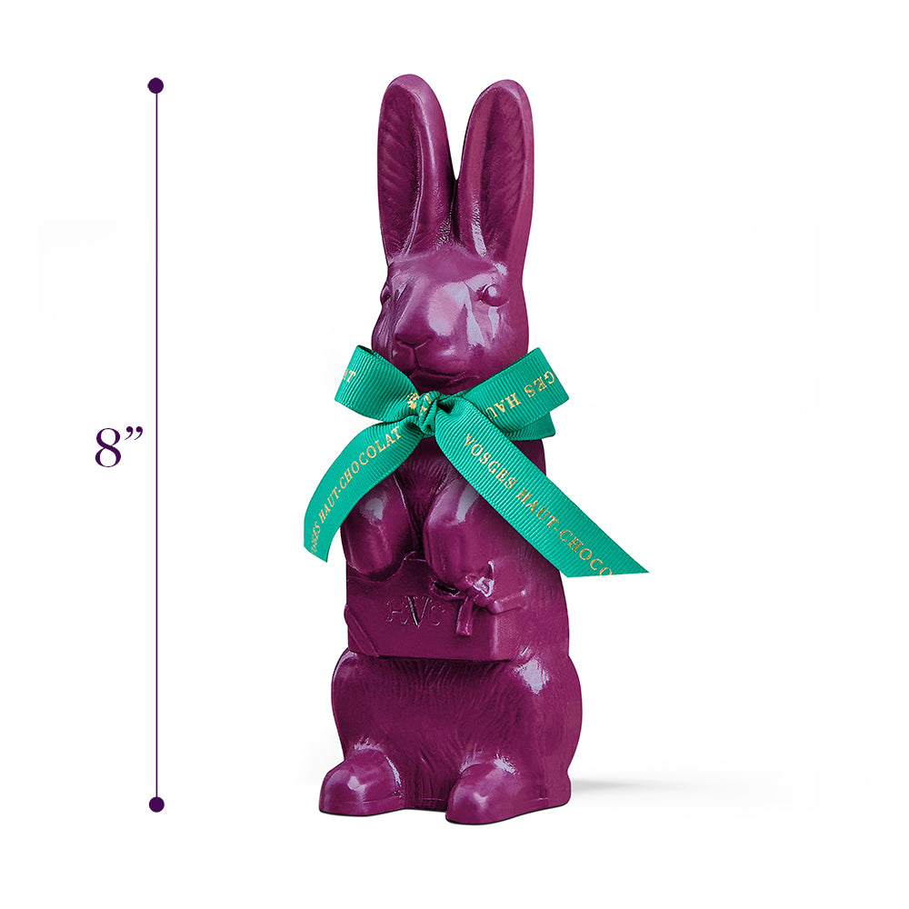 An eight inch tall, purple chocolate rabbit wearing a turquoise and gold ribbon bow stands upright on a white background beside product dimensions.