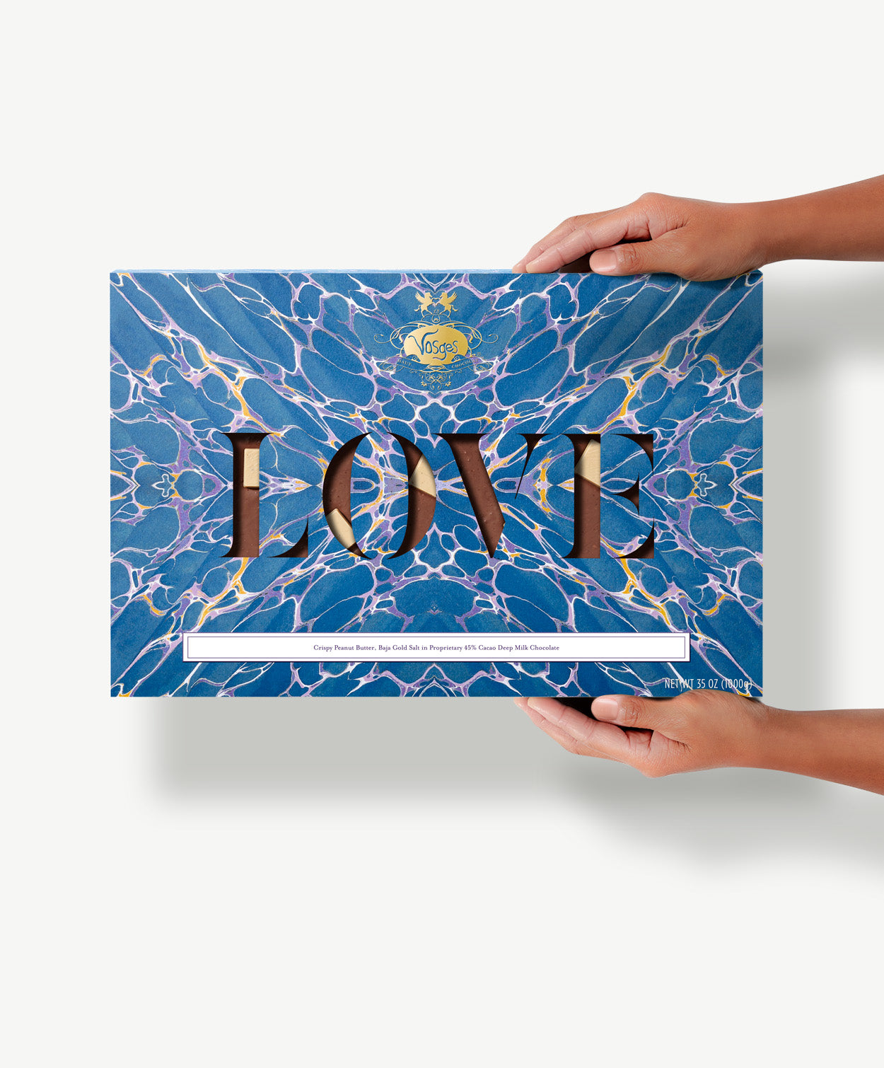 A gigantic two pound crispy peanut butter chocolate bar in a blue tie-dyed wrapper reading, "Love" held in a Caucasian woman's hands.  
