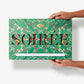 A gigantic two pound Sourdough Pretzel and Toffee Chocolate bar in a green, tie-dyed wrapper reading, "Soiree" held in a Caucasian woman's hands.