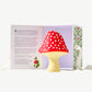 A large, white chocolate hazelnut mushroom decorated red with white spots standing in front an open white candy box painted with flowers.  