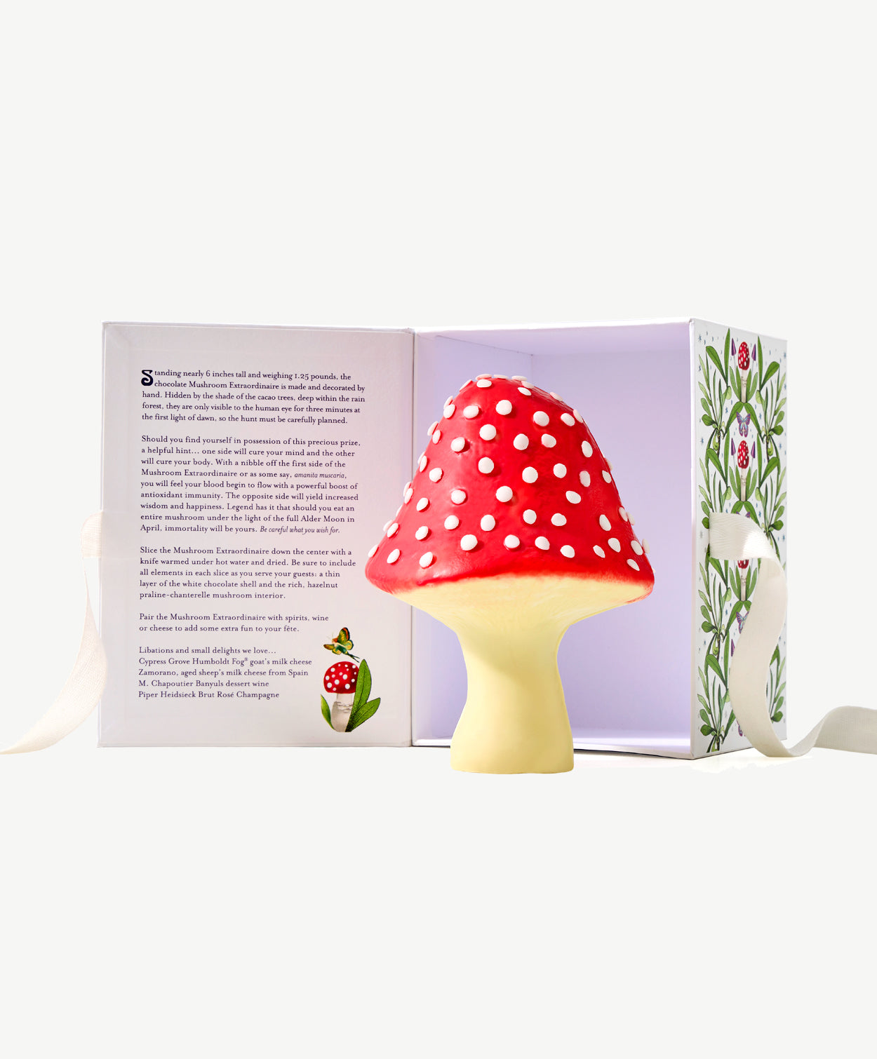 A large, white chocolate hazelnut mushroom decorated red with white spots standing in front an open white candy box painted with flowers.  