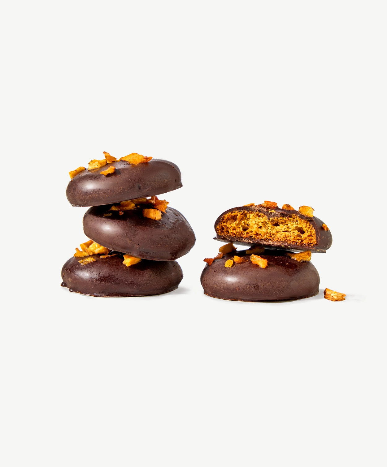 Two small stacks of Vosges Chocolate Dipped Cookies, one cut in half revealing a golden brown cookie adorned with dried persimmon on a grey background.