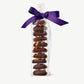 Tall stack of Vosges Chocolate Dipped Cookies topped with dried persimmons, in a clear plastic wrapper tied with a dark purple bow on a grey background.