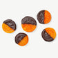 Five crystalized candied orange slices dipped in dark Vosges chocolate laying flat on a white background.