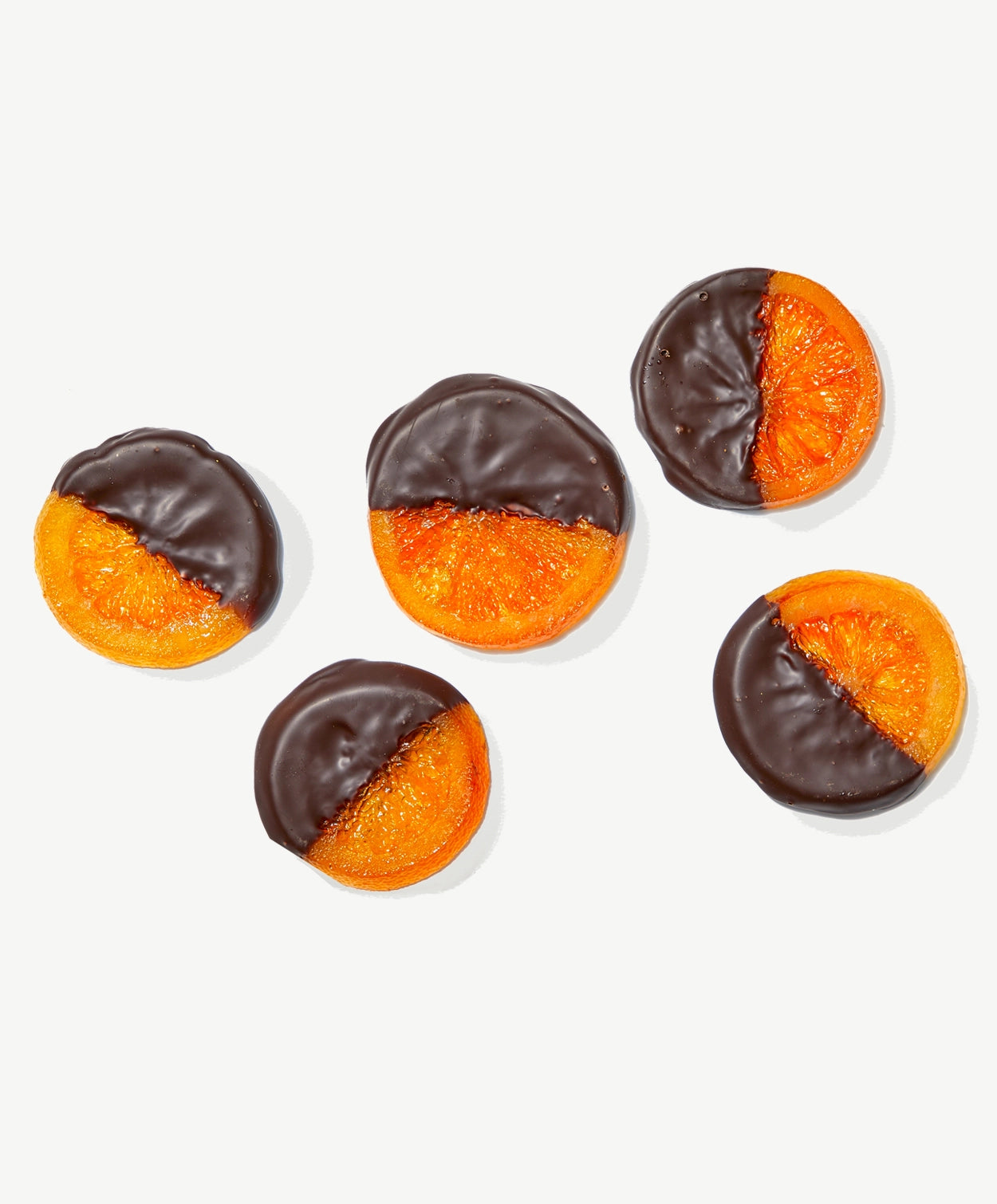 Five crystalized candied orange slices dipped in dark Vosges chocolate laying flat on a white background.