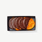 Several crystalized candied orange slices dipped in Vosges chocolate in a clear package on a grey background.