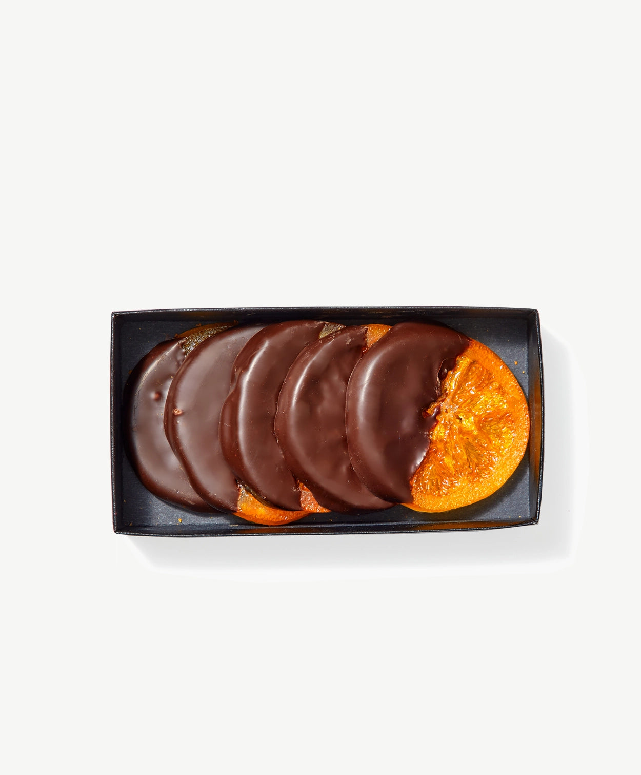 Several crystalized candied orange slices dipped in Vosges chocolate in a clear package on a grey background.