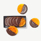 Several candied orange slices half dipped in dark Vosges chocolate sit beside and inside an opened package on a white background.