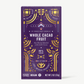 Vosges whole cacao fruit chocolate bar stands upright in a dark purple box  decorated with golden suns and moons on a grey background.