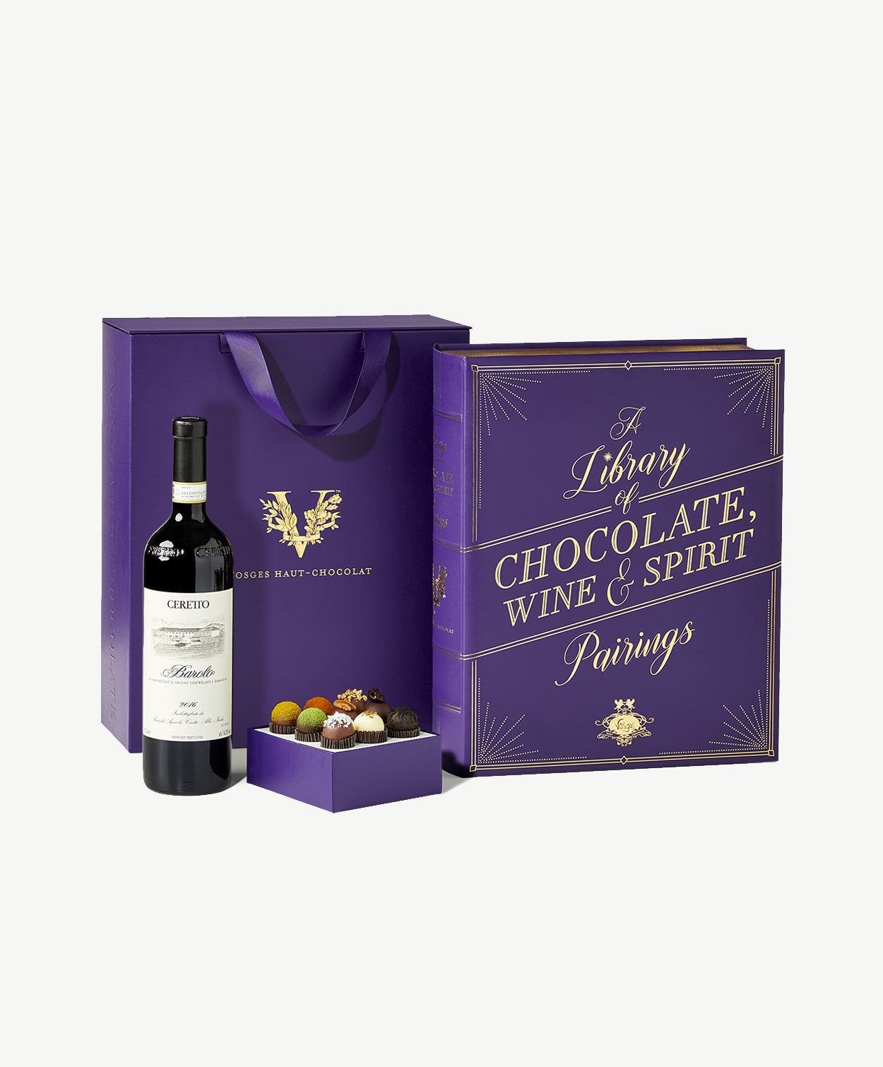A bottle of Ceretto red wine and an opened box of brightly decorated chocolate truffles sit beside a large purple candy box reading, "Chocolate, Wine & Spirit" on a grey background.
