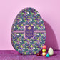 A small stack of colorful Vosges Chocolate truffles sit beside an egg shaped candy box decorated with green and purple dragons on a pink background.